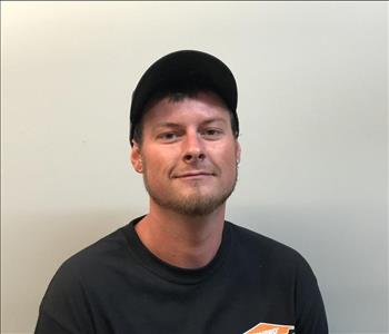 Headshot of half-smiling man wearing SERVPRO hat and uniform in front of gray background