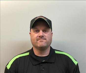 Headshot of half-smiling man wearing SERVPRO hat and uniform in front of gray background