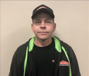 Headshot of half-smiling man wearing SERVPRO hat and uniform in front of gray background