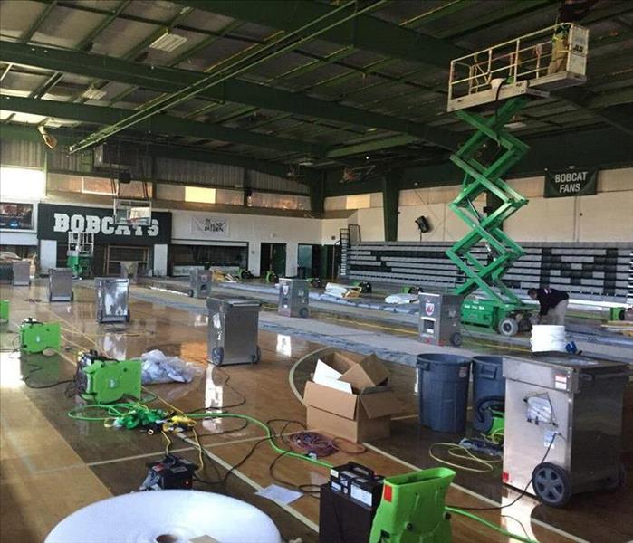 Green air movers and air scrubbers spread out in a poorly lit school gymnasium