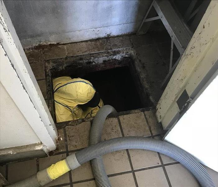 Person in yellow PPE holding a tube down into a crawlspace